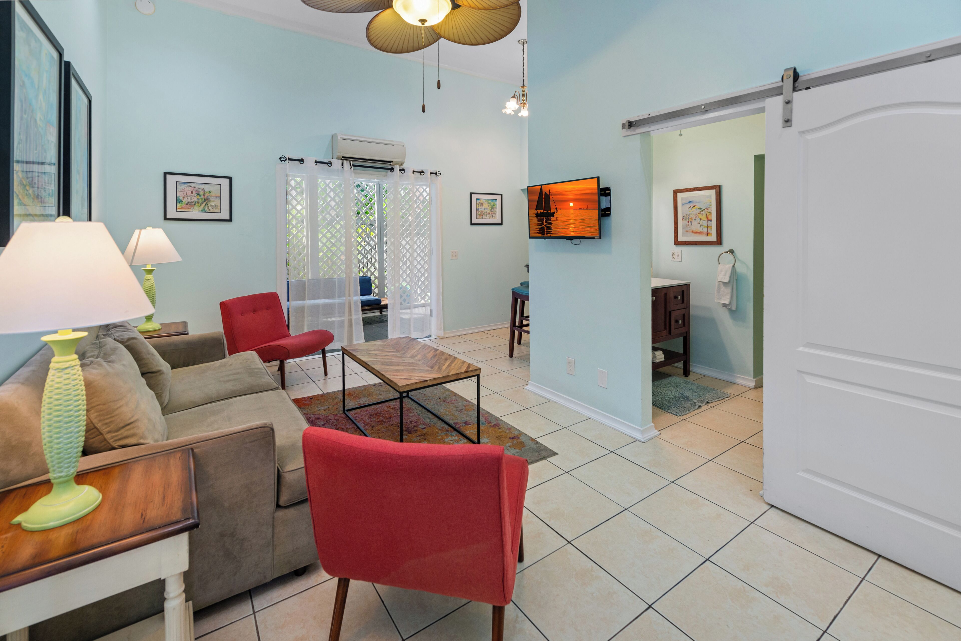 A living room with a sofa, red chairs, a coffee table, and a lamp. There is a sliding door leading to another room.