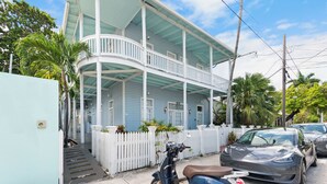 A two-story house with a porch, a white picket fence, and a parked scooter.