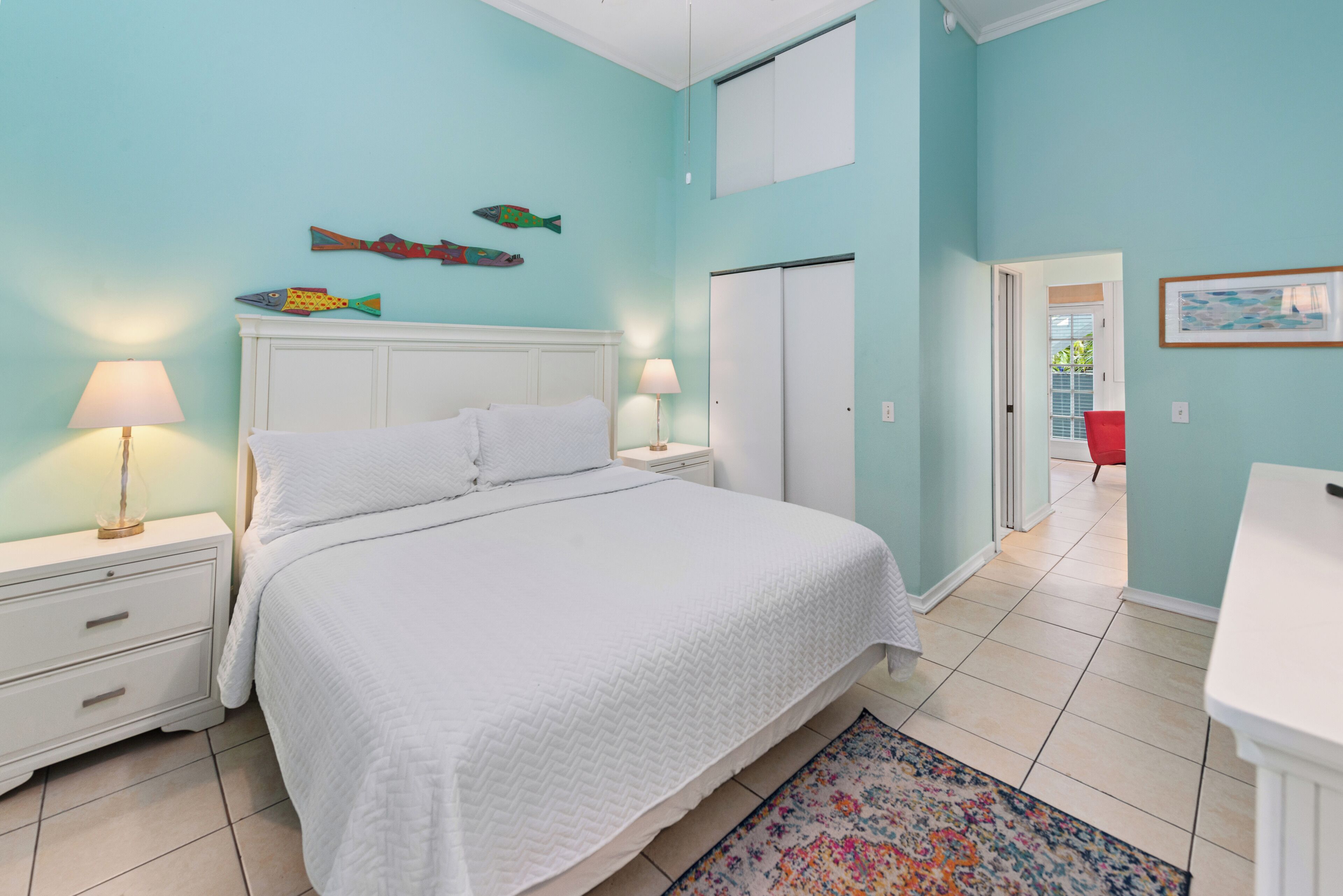 A bedroom with a bed, nightstands, a dresser, a mirror, and a door leading to another room.