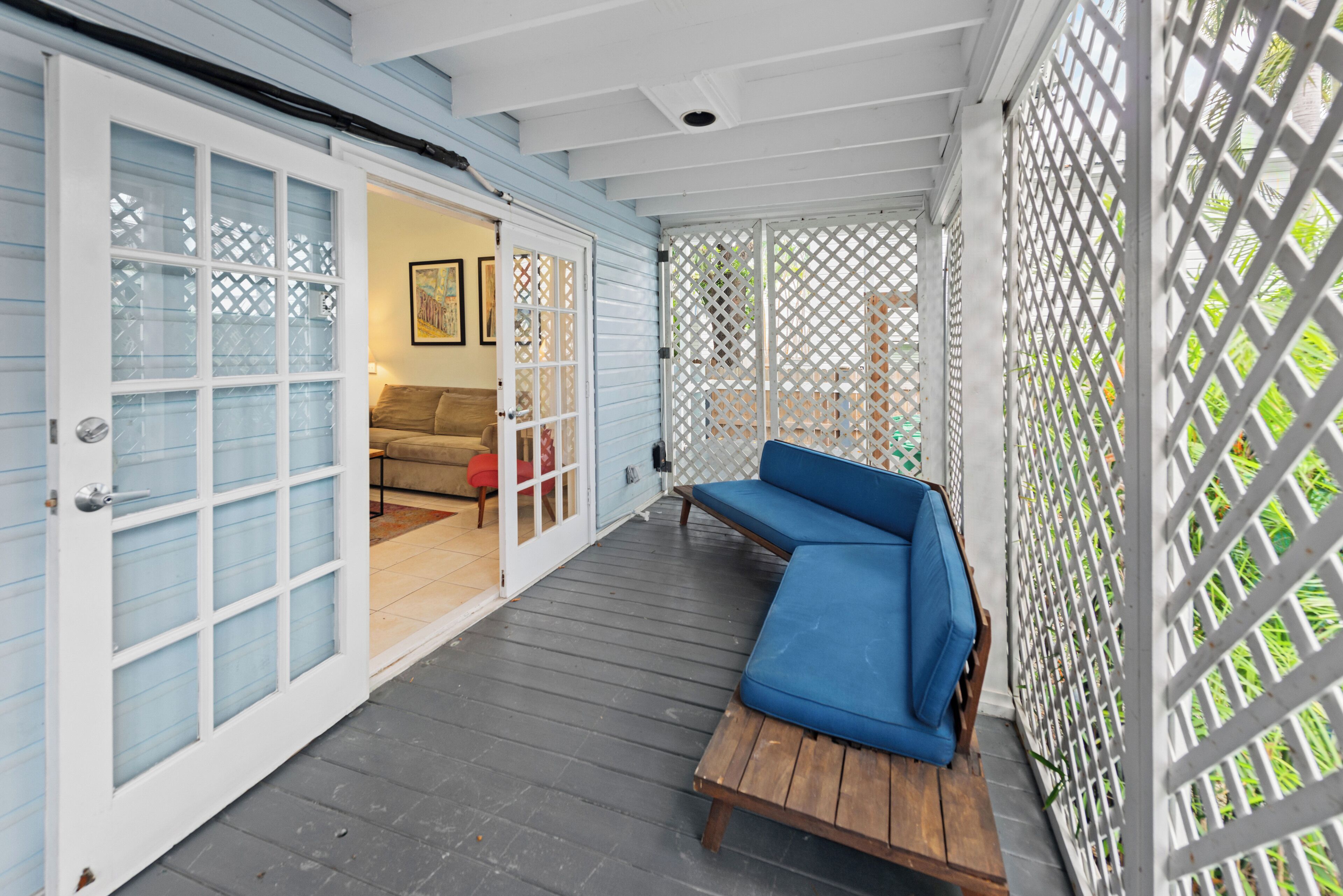 A covered porch with a blue sofa, a wooden bench, and a white lattice fence.