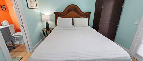 Una cama bien hecha con cabecera de madera, una lámpara de noche y un cuadro enmarcado en la pared.