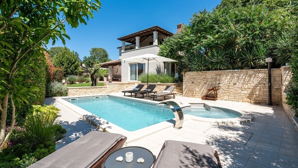 A two-story house with a swimming pool and a hot tub, surrounded by lush greenery.