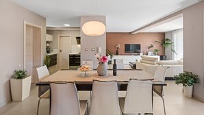 A modern dining area with a large table, chairs, a vase with flowers, and a hanging light fixture.