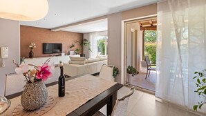 A modern living room with a sofa, a dining table with a vase and a bottle, and a TV mounted on the wall.