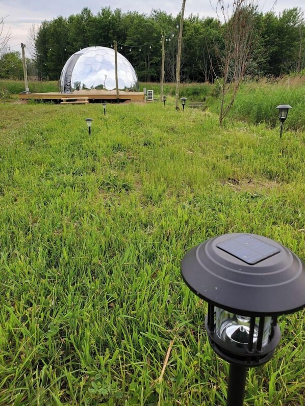 A grassy field with a spherical structure in the background and a solar-powered lamp in the foreground.
