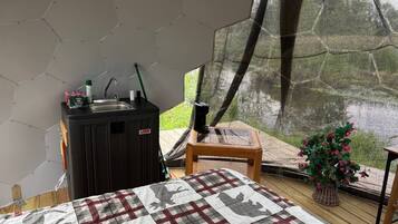 A room with a bed, a small table, a heater, and a window with a view of greenery.
