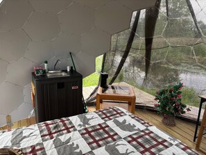 A room with a bed, a small table, a heater, and a window with a view of greenery. - Glamping Dome in Martville near Lake Ontario! (Martville)