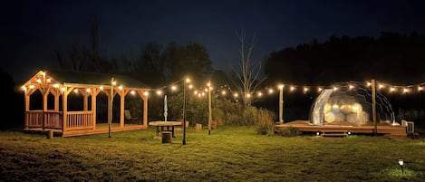 Un mirador con luces de cuerda, un espacio de estar techado y una estructura en forma de cúpula por la noche.
