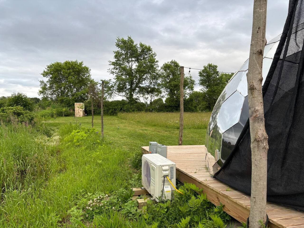 A tent set up in a grassy field with a wooden deck, surrounded by trees and a cloudy sky.