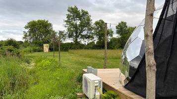 A tent set up in a grassy field with a wooden deck, surrounded by trees and a cloudy sky.