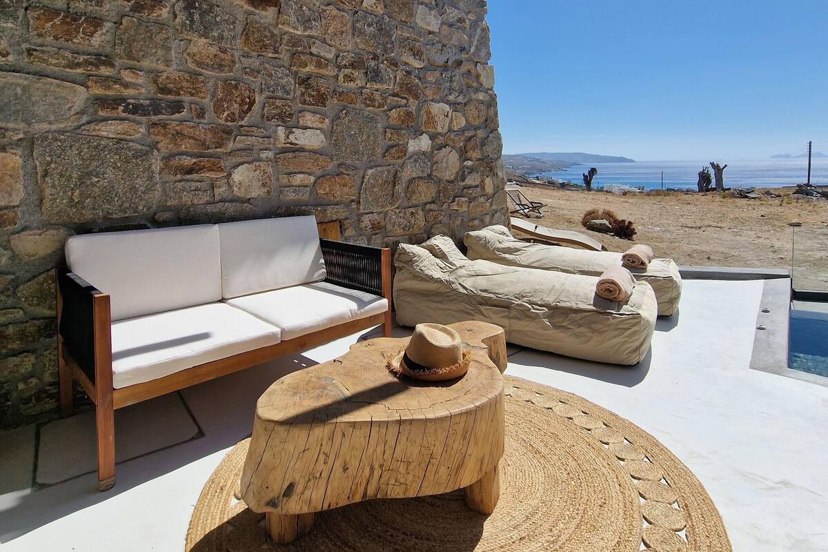 A stone wall, wooden furniture, and a poolside area with a view of the beach.