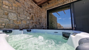 A stone-walled hot tub with a view of the landscape through a large window. - MvibesMykonos homes and studios (Mykonos)