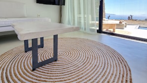 A modern room with a large window, a flat-screen TV mounted on the wall, a white sofa, and a round woven rug. - MvibesMykonos homes and studios (Mykonos)