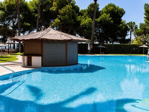 Una piscina con una pequeña estructura tipo cabaña, rodeada de árboles y un cielo despejado.