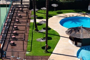 Un área de piscina en la azotea con sillones de descanso y sombrillas, rodeada de palmeras y un césped cuidado.