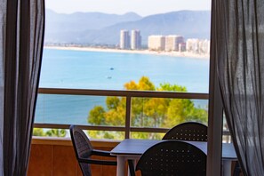Varanda com mesa e cadeiras, vista para uma praia e edifícios.