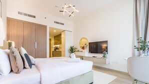 Un dormitorio moderno con una cama grande, un televisor y un baño visible a través de una puerta abierta.