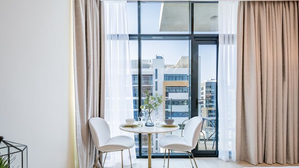 Un comedor moderno con una mesa redonda, dos sillas blancas y un jarrón con planta.