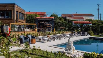 Zona de piscina con estatua de Buda, mobiliario exterior y restaurante con tejado de azulejos.