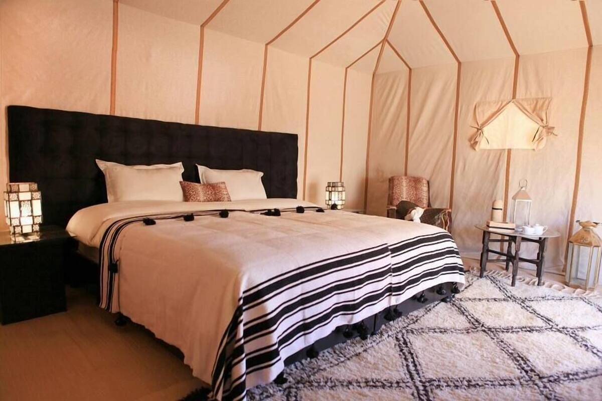 Un dormitorio con una cama grande, cabecera, mesitas de noche y una alfombra.