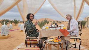 A desert tent with a dining table set for two, surrounded by decorative lanterns and palm trees.