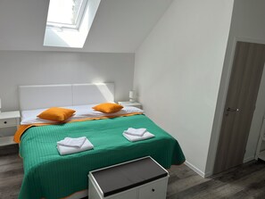 A neatly arranged bedroom with a bed, two pillows, a bedside table, a lamp, and a small white cabinet. - Stará vinice (Velke Zernoseky)