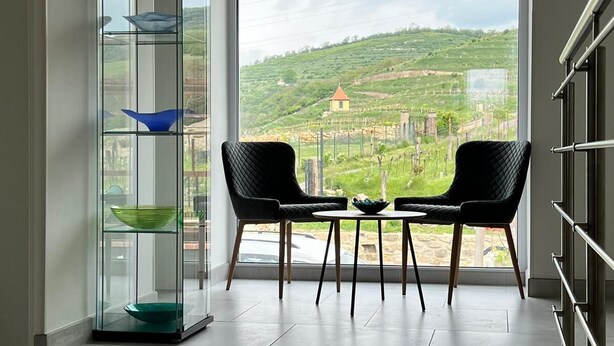 A modern room with a large window, two black chairs, a glass display unit, and a view of a green landscape. - Stará vinice (Velke Zernoseky)