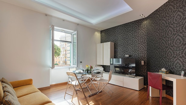 A modern living room with a sofa, a dining area with a glass table, and a kitchen with a TV. - Vernazzola Family Apartment (Genoa)