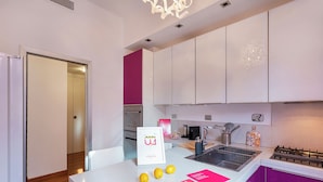 A modern kitchen with white and purple cabinets, a stainless steel sink, and a countertop with lemons and a welcome sign. - Vernazzola Family Apartment (Genoa)