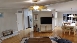 A spacious living room with hardwood floors, a ceiling fan, a flat-screen TV, a dining area with a table and chairs, and a bench. - RANCH WITH CACTUSES  Weekly/Monthly UP TO 50% OFF (Millsboro)