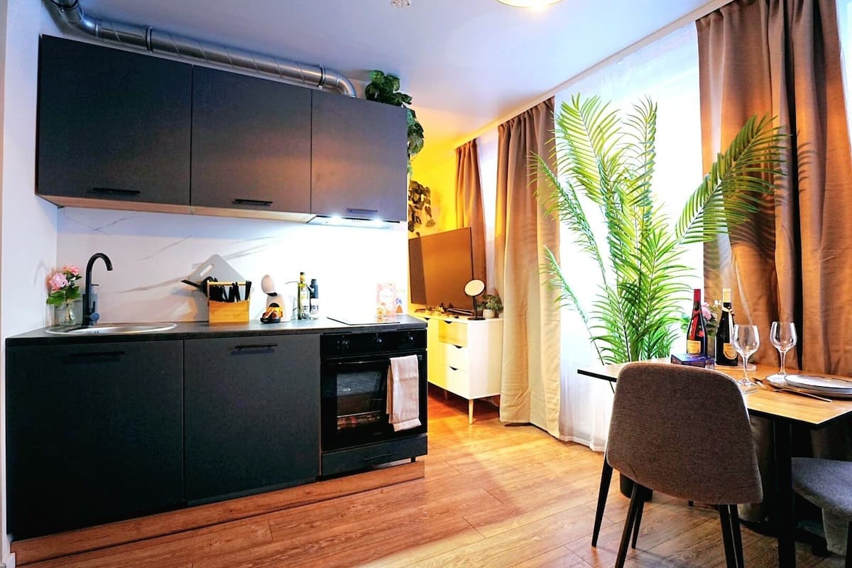 Une cuisine compacte avec des meubles de couleur sombre, un four encastré et un coin repas comprenant une table et des chaises.