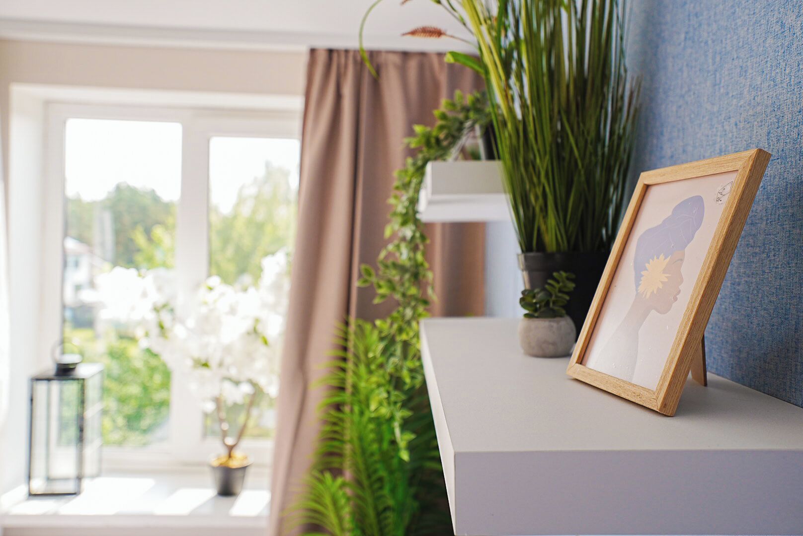 A room with a window, a potted plant, a framed picture, and a lamp on a table.