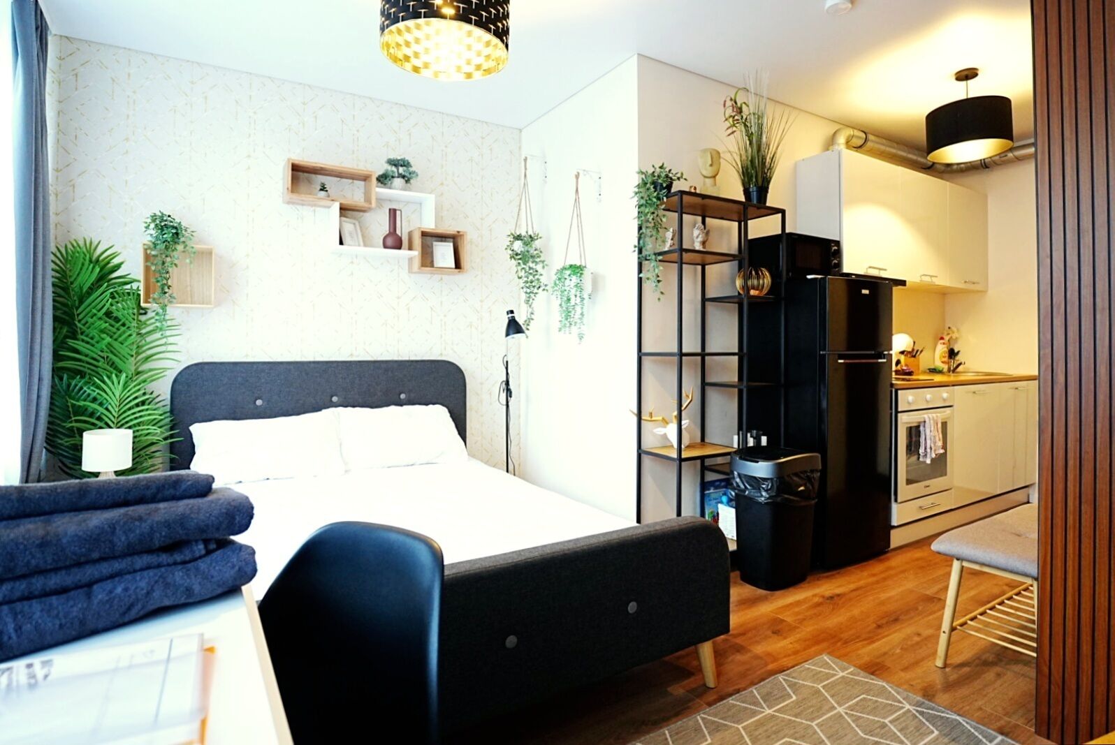Une chambre moderne comprenant un lit, des tables de chevet, un bureau et une chaise. Il y a également un coin cuisine avec un réfrigérateur, un four et un évier.