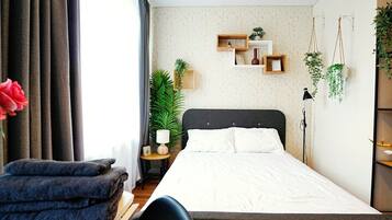 Un dormitori modern amb un llit gran, una taula de nit amb una làmpada, una petita planta i una estant mural amb elements decoratius.