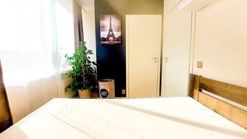 A bedroom with a bed, a potted plant, a door, and a wall with a picture.
