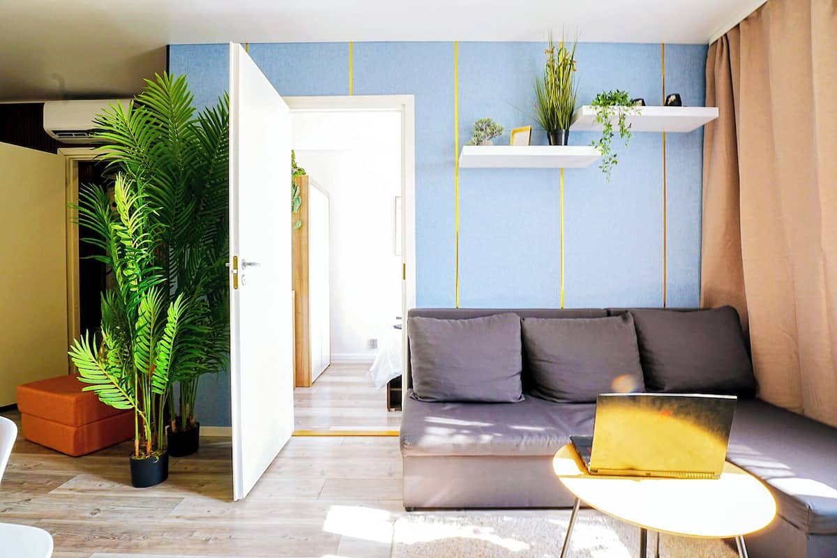 Un salon moderne avec un canapé, une table basse et un ordinateur portable. On y trouve également des plantes en pot et un couloir qui mène à une autre pièce.