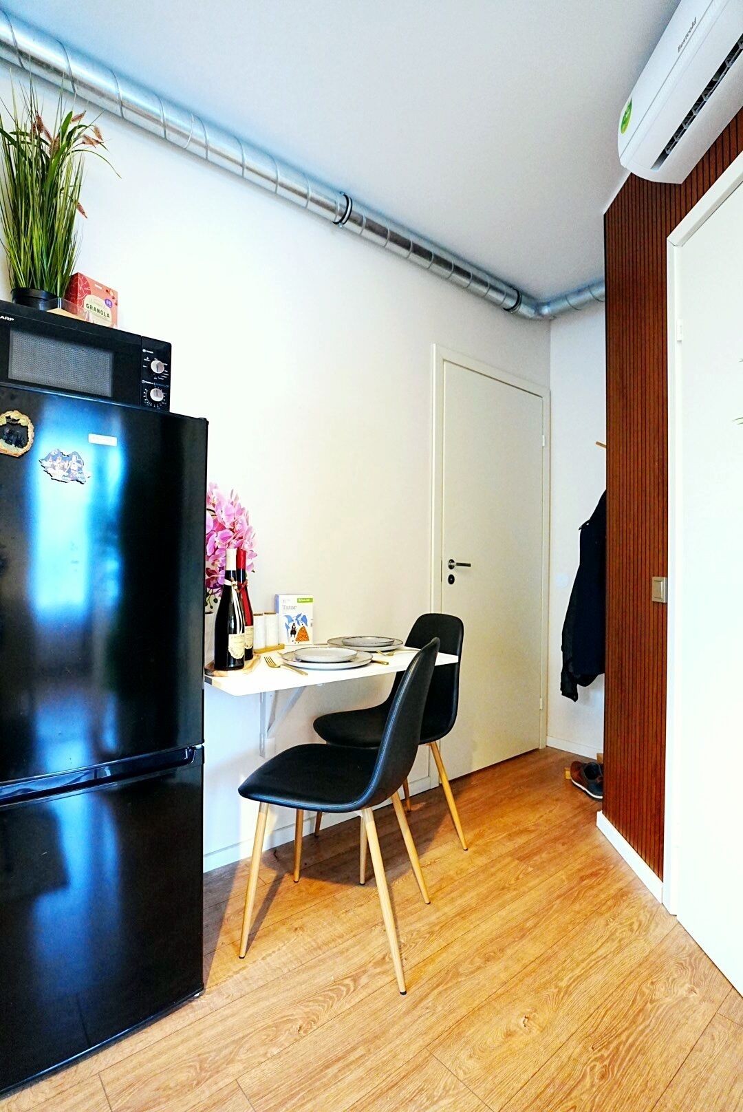 Una cocina compacta con un refrigerador negro, una mesa de madera con dos sillas y una puerta blanca.