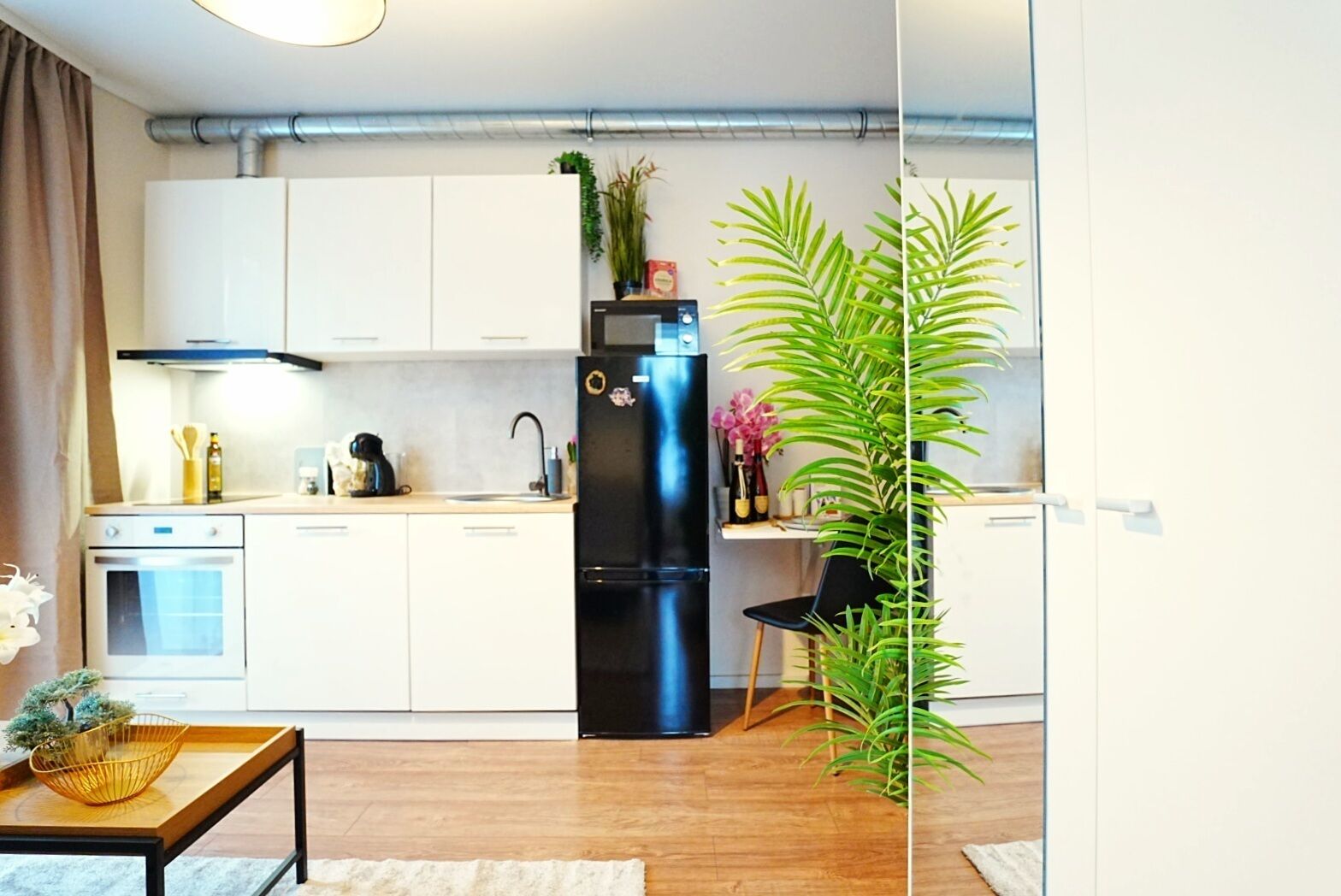 A modern kitchen with white cabinets, a black refrigerator, and a wooden dining table.