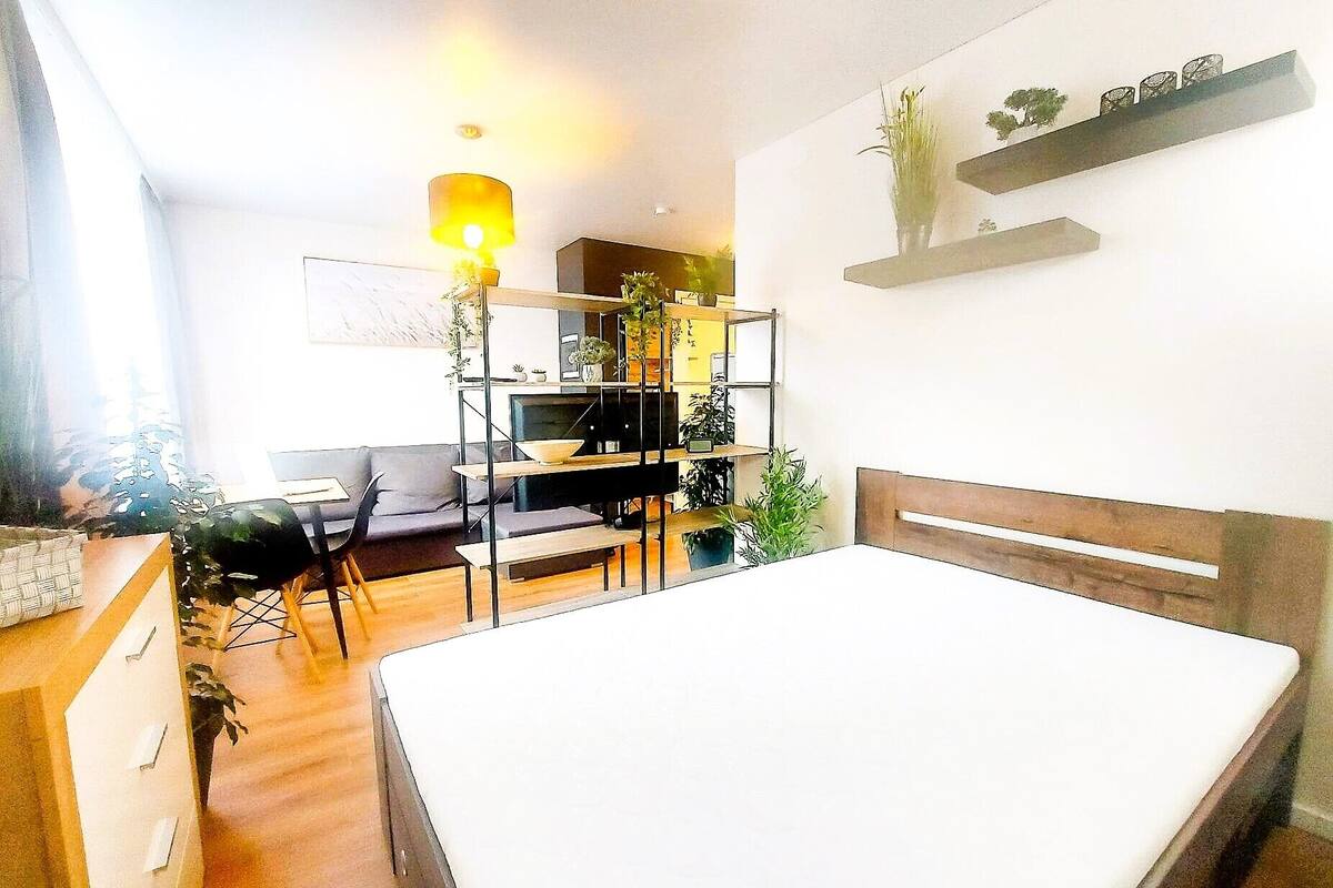 Une chambre à coucher moderne avec un lit, un bureau et une chaise. On y trouve une étagère avec des plantes et une lampe.