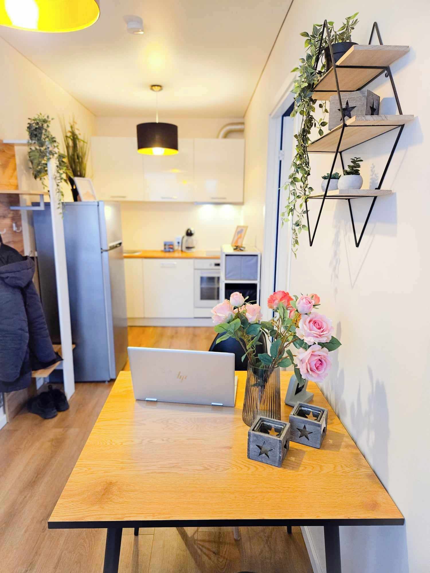 A modern kitchen with a wooden table, a laptop, and decorative items including a vase with flowers and star-shaped containers.