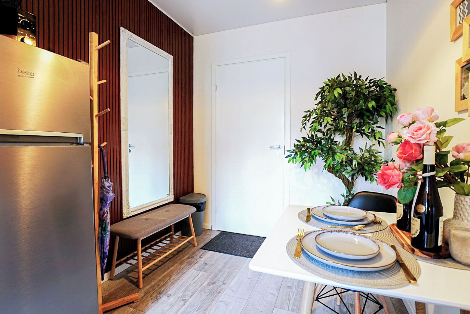 A compact kitchen with a built-in refrigerator, a bench, and a dining table set for two with plates and cutlery.