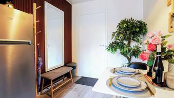 A compact kitchen with a built-in refrigerator, a bench, and a dining table set for two with plates and cutlery.