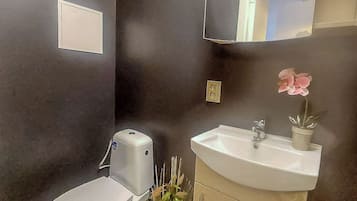 Un baño con inodoro, lavamanos, espejo y una pequeña planta en maceta.