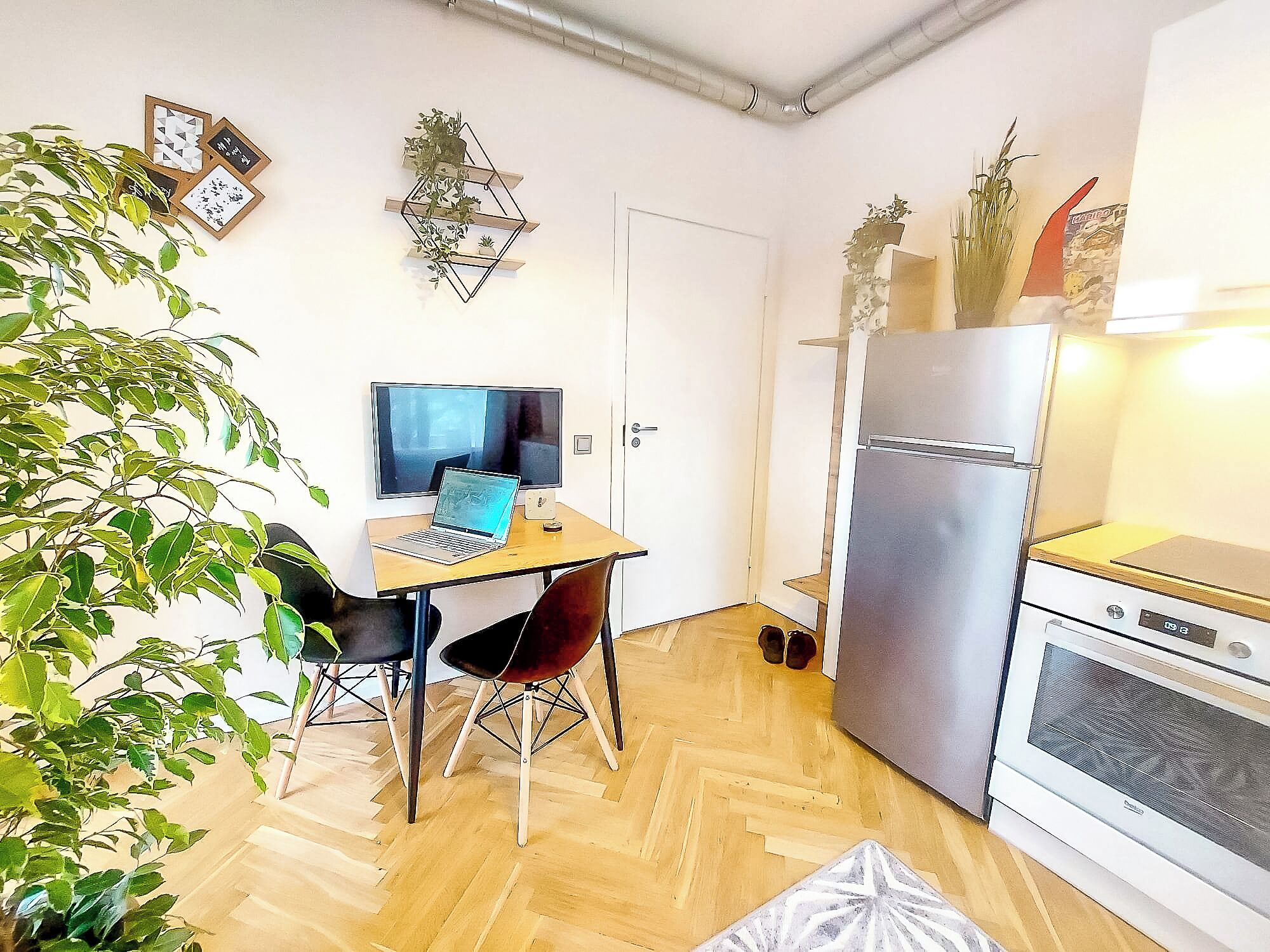 Une cuisine de taille réduite avec une table à manger en bois, un ordinateur portable et un réfrigérateur.