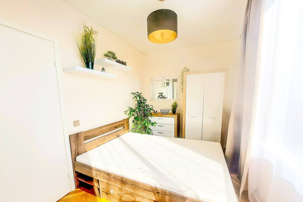 Une chambre à coucher avec un lit en bois, une commode, un miroir et une plante suspendue.