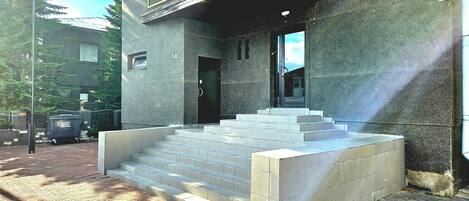 A building with a concrete facade, a metal balcony, and a set of stairs leading to the entrance.