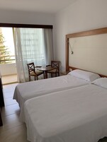 A hotel room with two beds, a small table with chairs, and a balcony with a view.