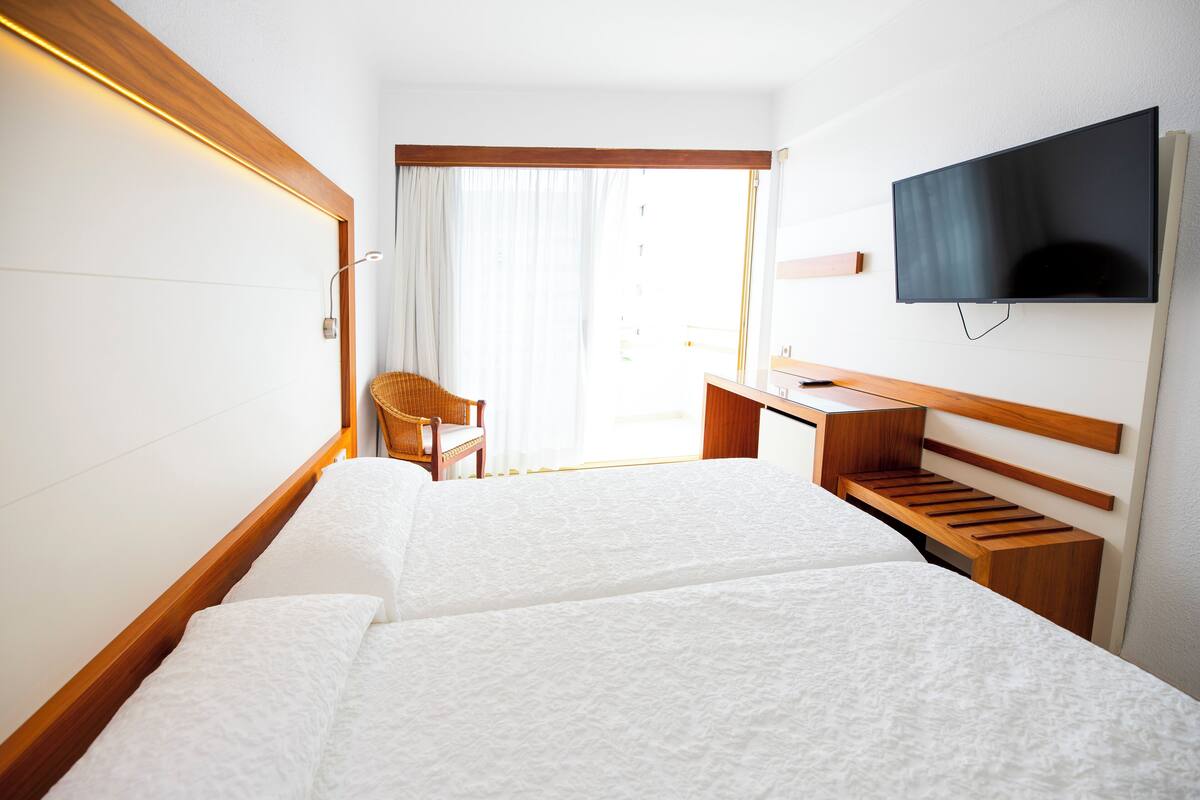 A hotel room with a bed, a desk, a chair, and a TV mounted on the wall.