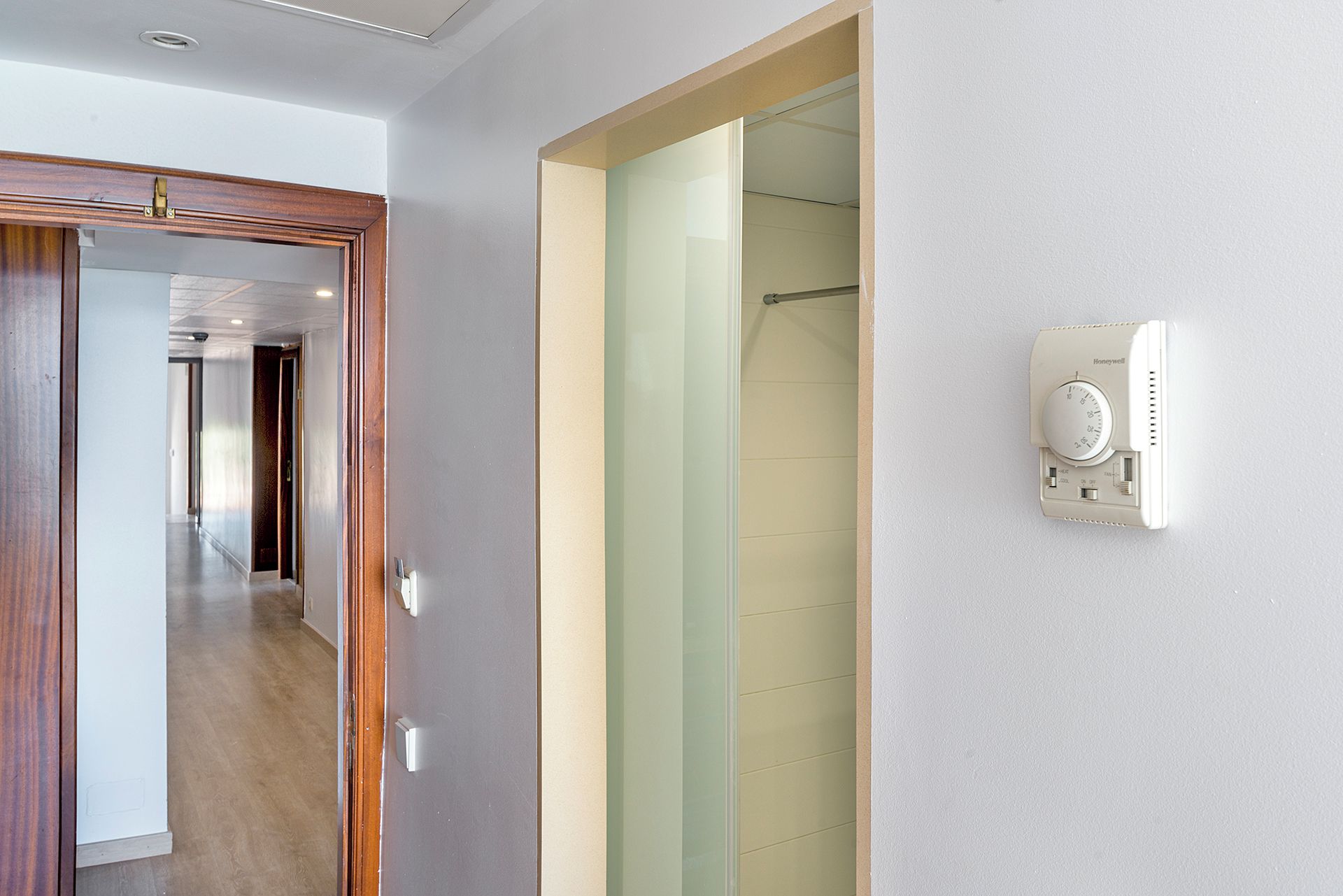 Habitación de hotel con puerta de madera, cabina de ducha de vidrio y un termostato Honeywell en la pared.