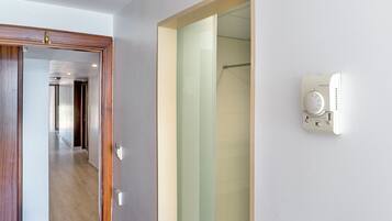 Habitación de hotel con puerta de madera, cabina de ducha de vidrio y un termostato Honeywell en la pared.